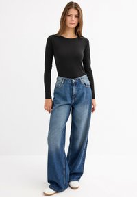 Top negro de manga larga combinado con jeans de mezclilla azul de pierna ancha y cintura alta. Presenta un diseño simple, textura ligera y un tono azul clásico.
