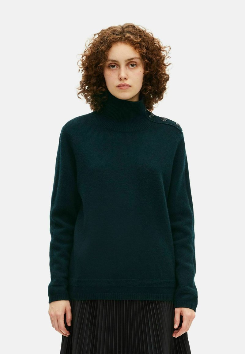 Mørkegrøn turtleneck sweater i et blødt, struktureret stof, med ribbede manchetter og en knapdetalje på venstre skulder.