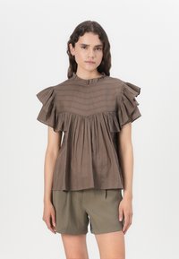 Bruine blouse met korte mouwen, versierd met ruches, een hoge halslijn en verticale strepen structuur, gecombineerd met olijfgroene shorts.