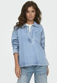 Suéter de mezclilla azul claro con un cuello bajo, un bolsillo y un ajuste relajado. Presenta mangas largas y una textura suave. Combinado con jeans a juego.