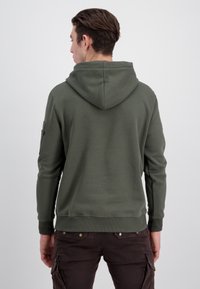 Felpa con cappuccio verde oliva, con una vestibilità comoda, polsini e orlo a coste, e una tasca laterale con zip. Texture liscia.