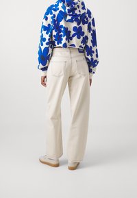 Sudadera recortada con un patrón floral azul sobre fondo blanco, combinada con pantalones de pierna ancha en color crema y zapatillas ligeras, cuenta con bolsillos traseros.