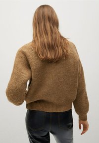 Pull marron tricoté avec une finition texturée, coupe décontractée, et ourlet côtelé, porté sur un pantalon en cuir synthétique noir.