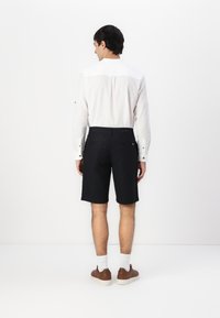 Černé šortky vyrobené z látky, spárované s bílou košilí s dlouhým rukávem. Košile má jednoduchý design s knoflíkovými detaily.