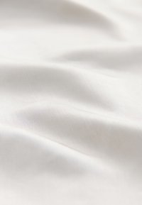 Tela blanca suave con una textura lisa, que muestra ondas suaves y un brillo sutil, destacando su calidad liviana y su capacidad para caer con elegancia.