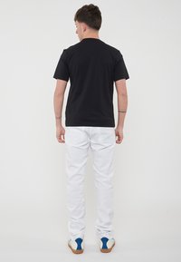 T-shirt nera a maniche corte abbinata a pantaloni bianchi. La maglietta ha un classico collo rotondo ed è realizzata in un tessuto liscio. I pantaloni hanno tasche posteriori.