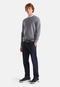 Maglione grigio a maniche lunghe abbinato a jeans in denim blu scuro e sneakers nere. Il maglione ha un collo rotondo; i jeans hanno una vita aderente.