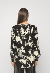 Blouse à motifs floraux noirs et crème avec manches longues, large encolure et ourlet légèrement courbé. Confectionnée dans un tissu doux et texturé.