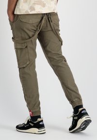 Pantalones cargo color caqui con piernas ajustadas, múltiples bolsillos laterales y puños de tobillo ajustables, combinados con zapatillas negras y grises.