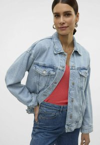 Svetlo modra oversize denim jakna z dvema sprednjima žepoma, srebrnimi gumbki in sproščenim fit-om, nosi se čez koralni rebrasti top.