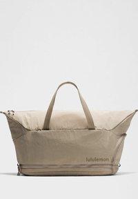 Beige tygväska med triangulär design, dubbla sidodragkedjor och två handtag upptill. Har "lululemon"-logotypen på sidan.