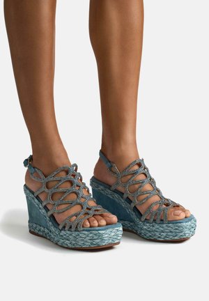 Sandalias cuña azules con una base trenzada, que presentan un diseño con tiras adornadas con acentos metálicos y puntera abierta.
