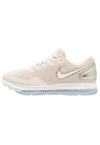 Chaussure de course Nike beige clair avec tige en mesh, logo swoosh blanc, semelle rembourrée et semelle extérieure en caoutchouc bleu translucide.