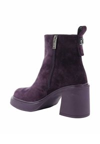 Fioletowe zamszowe botki za kostkę na grubej podeszwie, z bocznym zamkiem błyskawicznym i uchwytem do zakupu. Kształt jest smukły z zaokrąglonym noskiem.