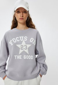 Sudadera de color púrpura claro con texto blanco y diseño de estrellas. Presenta un escote redondo y un corte relajado. Textura suave con puños acanalados.