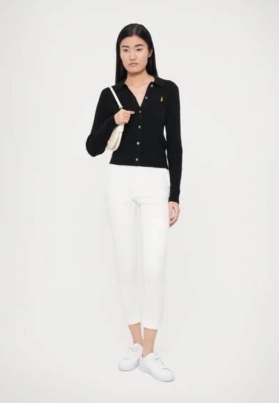 Čierny rebrovaný kardigán s golierom a zapínaním na gombíky, kombinovaný s bielymi úzkymi džínsami a bielymi teniskami. Nosená je minimalistická kabelka.