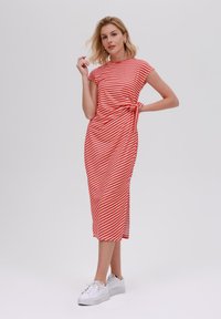 Robe midi rayée rouge et blanche avec des manches courtes, ceinturée à la taille et dotée de fentes sur les côtés, associée à des baskets blanches. Tissu lisse et léger.