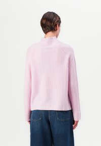 Pulover tricotat cu model în dungi, de culoare roz, cu gât înalt, umeri lăsați și o croială confortabilă, asortat cu blugi evazați de culoare albastru închis.