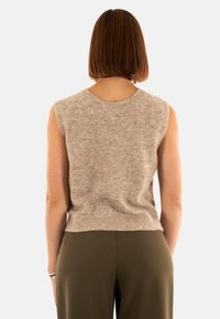 Top senza maniche beige in maglia con una morbida texture e orlo a costine, indossato con pantaloni a gamba larga verde oliva. Vista posteriore.