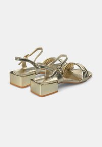 Sandali slingback metallici oro con tacco a blocco. Presentano sottili cinturini e un design plissettato sulla parte superiore. Texture liscia, suola piatta.
