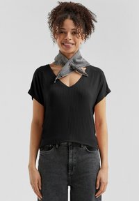 T-shirt nera a coste con scollo a V e maniche corte, abbinata a una sciarpa in denim grigia annodata attorno al collo, indossata con jeans grigi scuri.