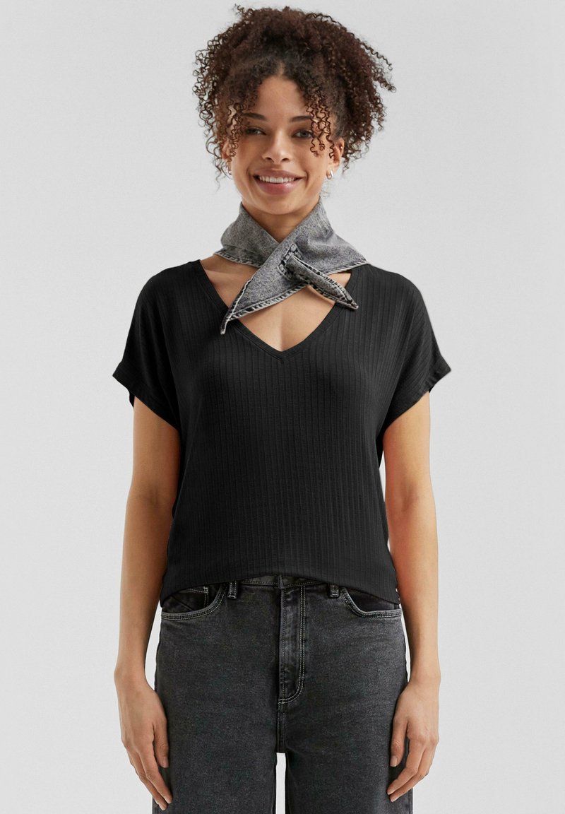 T-shirt nera a coste con scollo a V e maniche corte, abbinata a una sciarpa in denim grigia annodata attorno al collo, indossata con jeans grigi scuri.