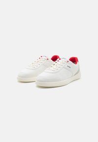White sneakers with a smooth surface, featuring red accents at the heel, beige sole, and a textured stripe on the sides. Logo visible.
