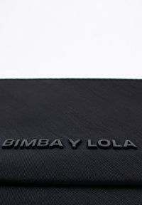 Must mustkott, millel on tekstureeritud pind ja musta värviga väljaulatuv brändinimi "BIMBA Y LOLA". Lihtne, ristkülikukujuline disain ilma lisade või aktsentideta.