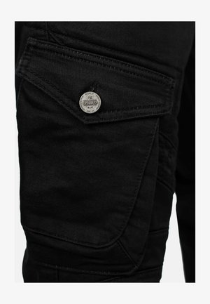 Zwarte denim cargo-broek met een gestructureerde afwerking, voorzien van een grote zijzak, zilveren logo-accessoires en opvallende stiksels.