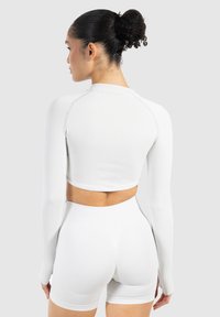 Top court à manches longues côtelé blanc et shorts taille haute, présentant un design ajusté et une texture sans coutures, vu de dos.