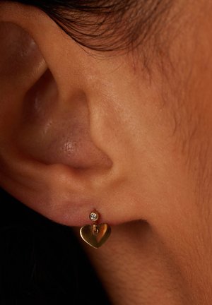 Gouden hartvormige oorbel met een kleine edelsteenaccent, hangend aan een eenvoudige post. Close-up detail van het oorlepel.