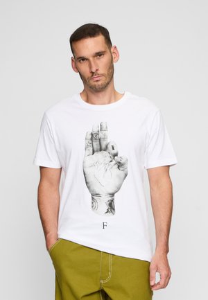 T-shirt en coton blanc présentant un graphique noir d'une main tatouée. Le design comprend des éléments détaillés sur les doigts et la paume.