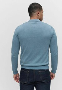 Tajtat blå tröja med lång ärm, ribbade manschetter och nederkant, samt en klassisk kragsdesign, parat med mörka jeans.