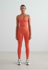 Set di activewear corallo composto da un top halter con scollatura a V e dettaglio con foro, abbinato a leggings aderenti a vita alta.