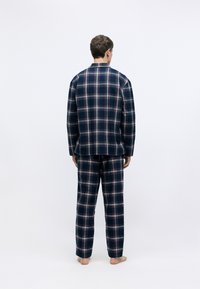 Conjunto de pijama a cuadros en azul marino con detalles en rojo y blanco. Tejido suave, de mangas largas y pantalones de corte relajado. Diseño minimalista, sin marcas visibles.