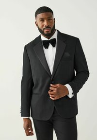 Sort smoking med satinrevers, hvid skjorte med plisseringer, sort butterfly og et enkelt lommetørklæde. Tekstureret stof, skræddersyet pasform.