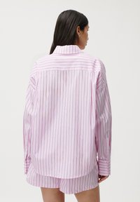 Camicia a maniche lunghe in morbido cotone rosa pallido con sottili righe nere verticali, con colletto a punta e polsini a bottoni, vista da dietro.