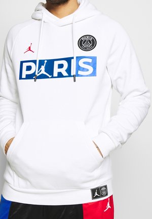 Biała bluza z kapturem z niebieskim napisem "PARIS" z logo Jumpman, odznaką Paris Saint-Germain na piersi oraz dopasowane szorty z czerwonym, czarnym i niebieskim panelem.