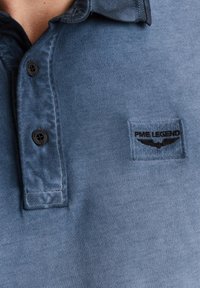 Camicia di jeans blu con finitura texture, dotata di un logo PME Legend nero sul petto e due bottoni neri al colletto.
