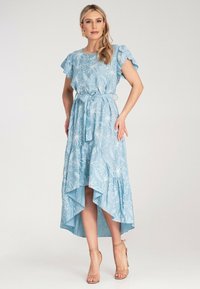 Jasnoniebieska maksidługa sukienka z falbankami przy krótkich rękawach, białym floralnym wzorem, zawiązywanym paskiem w talii i asymetrycznym dołem. Gładka tekstura.
