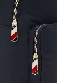 Närbild av två guldblixtlås på mörk tyg, var och en med en dragkedja som har diagonala vita, röda och marinblå ränder.