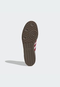 Semelle en caoutchouc marron avec une surface texturée et des détails circulaires. Présente trois cercles surélevés et le logo "adidas".
