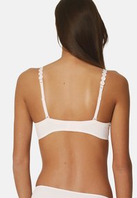Sujetador blanco con tirantes en forma de acordeón, una banda inferior suave y un tejido blando y elástico, diseñado para brindar comodidad y soporte.