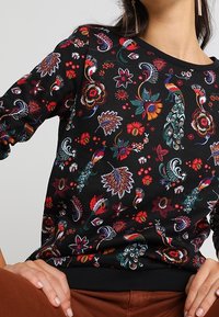 Sudadera negra con estampados florales coloridos y de pavo real, con cuello redondo y pu�ños acanalados. Textura suave y diseño de ajuste holgado.