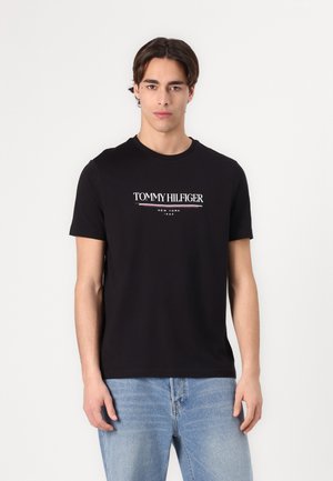Schwarzes Baumwoll-T-Shirt mit kurzen Ärmeln, das ein weißes Logo "TOMMY HILFIGER" und "NEW YORK 1985" in einer fetten Schriftart auf der Vorderseite zeigt.