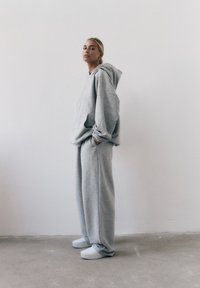 Szary, oversize'owy hoodie wykonany z miękkiej bawełny, zestawiony z luźnymi spodniami dresowymi. Zestaw charakteryzuje się swobodnym krojem i prostym designem.