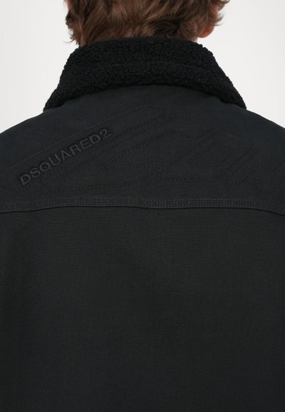 Black jacket with a sherpa collar, featuring embossed “DSQUARED2” logo on the back. Textured fabric with a clean, modern design.
