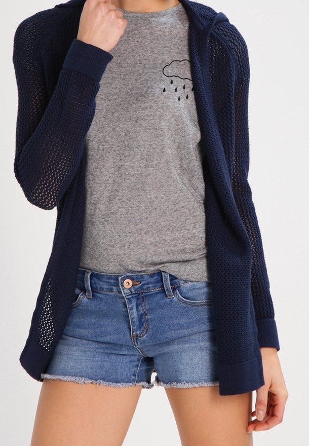 Granatowy dzianinowy kardigan o teksturowanym, otwartym splocie, zestawiony z szarą koszulką z grafiką chmury oraz niebieskimi dżinsowymi szortami.