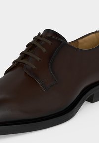 Gros plan d'une chaussure habillée en cuir marron foncé poli avec des lacets et une semelle noire.