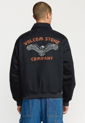 Sort bomberjakke med et grafisk design med en ørn og teksten "VOLCOM STONE COMPANY" i orange på ryggen. Ribbet manchetter og talje.
